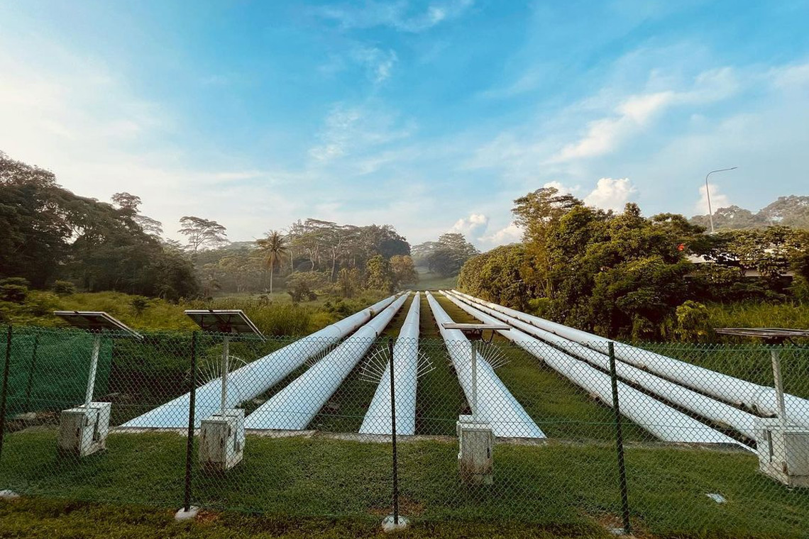 Jalur Pipeline Trail dengan hamparan rumput luas dan pipa-pipa besar.